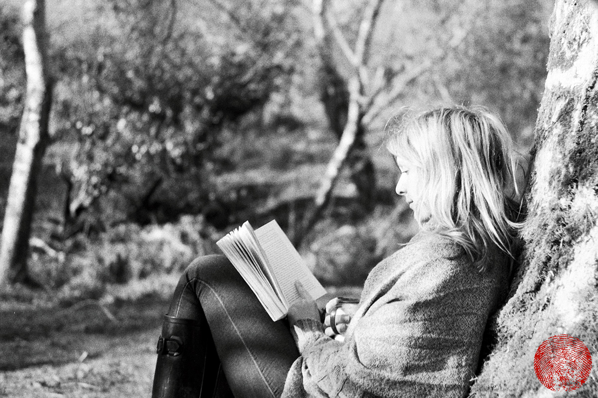 lady leaning against a tree trunk reading a book, shot with a zorki 4k rangefinder vintage camera
